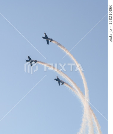 Three aerobatic aircraft performing a synchronized aerial maneuver with curved smoke trails against a clear blue sky during an aviation airshow. Dynamic formation display in an open sky background 138210866