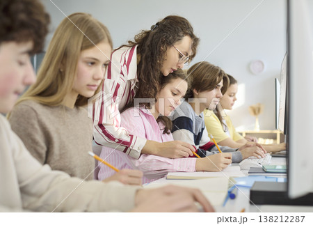 Teacher guiding teens on computers in modern classroom for collaborative learning 138212287
