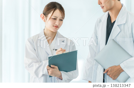 病院の通路で会話する医者・医師・医療従事者・ドクター・薬剤師・科学者・研究員の男女 病院の通路で会話する医者・医師・医療従事者・ドクター・薬剤師・科学者・研究員の男女 138213347