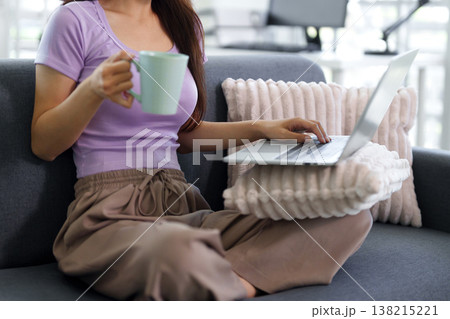 Asian adult woman using laptop computer working online home sofa holding mug relaxing comfortable remote work freelancer digital lifestyle Asian adult woman using laptop computer working online home sofa holding mug relaxing comfortable remote work freelancer digital lifestyle 138215221