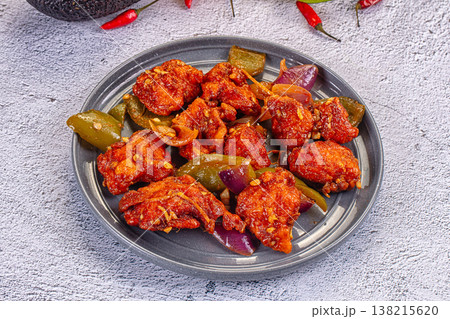 Spicy red chicken 65 appetizer with onions in a bowl, surrounded by fresh chili, avocado, and peppers. Spicy red chicken 65 appetizer with onions in a bowl, surrounded by fresh chili, avocado, and peppers. 138215620