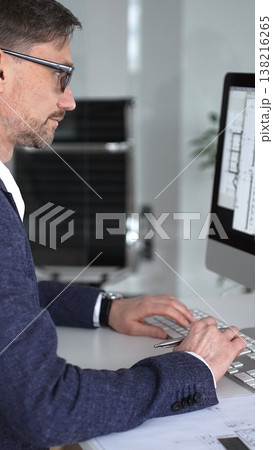 Architect designing building plans on computer, typing at desk with architectural model and blueprints. Business and architecture concept 138216265