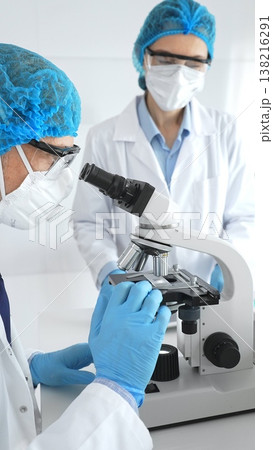 Scientists researchers man and woman in lab coats, masks and goggles conduct research with microscope in laboratory. Concept of medicine and science 138216291