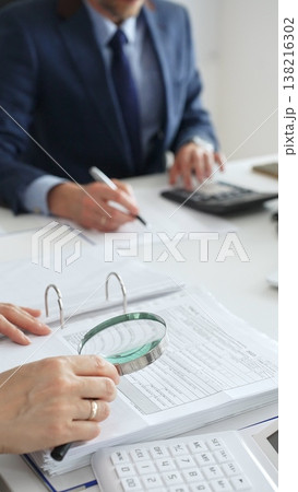 Financial analysts examining documents, using magnifying glass and calculator while studying corporate data at workplace. Audit and taxes in business Financial analysts examining documents, using magnifying glass and calculator while studying corporate data at workplace. Audit and taxes in business 138216302
