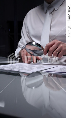 Business person examining a document using a magnifying glass, focusing on fine print and terms in a legal agreement, working late. Audit and overworking concepts 138216321
