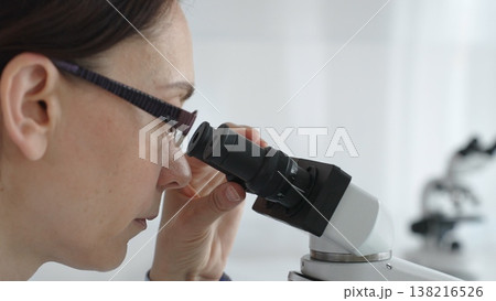 Female researcher focusing on a microscope lens, analyzing scientific samples in a sterile lab for medical innovations. Medicine and science concept Female researcher focusing on a microscope lens, analyzing scientific samples in a sterile lab for medical innovations. Medicine and science concept 138216526