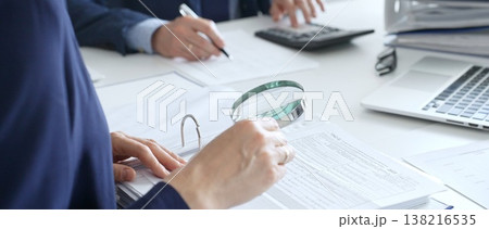 Close up of female accountant hands using calculator and magnificent glass while collaborating with male colleague in office, calculating taxes and analyzing financial data. Audit and taxes in Close up of female accountant hands using calculator and magnificent glass while collaborating with male colleague in office, calculating taxes and analyzing financial data. Audit and taxes in 138216535
