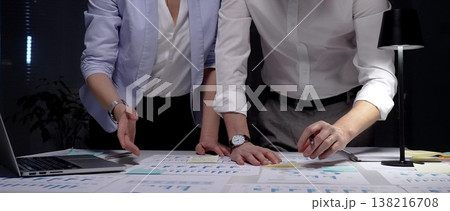 Business professionals collaborating on a data analysis project, reviewing financial reports and marketing strategies late in the evening to achieve corporate growth and success 138216708