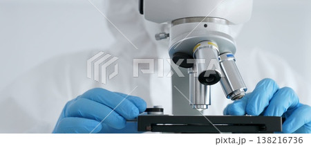 Close up of scientific researcher or virologist wearing protective gear is adjusting microscope, analyzing lab samples with precision in sterile research environment. Medicine and science concept Close up of scientific researcher or virologist wearing protective gear is adjusting microscope, analyzing lab samples with precision in sterile research environment. Medicine and science concept 138216736