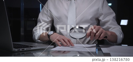 Person examining a document using a magnifying glass, focusing on fine print and terms in a legal agreement, working late. Audit and overworking concepts Person examining a document using a magnifying glass, focusing on fine print and terms in a legal agreement, working late. Audit and overworking concepts 138216780
