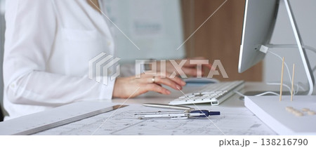 Architect creating new designs, working at a computer in office with blueprints and drafting tools. Business and architecture concept 138216790
