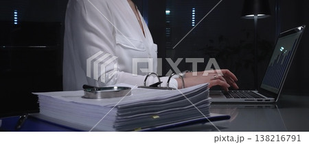 Businesswomen working overtime in a dark office, typing on laptop with financial charts and data reports on desk at night. Audit and taxes in business Businesswomen working overtime in a dark office, typing on laptop with financial charts and data reports on desk at night. Audit and taxes in business 138216791
