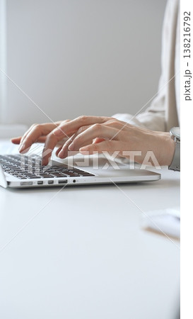 Professional businesswoman working intently on laptop, wearing tailored beige suit and silver watch, seated at minimalist white desk in modern office environment. Business people concept Professional businesswoman working intently on laptop, wearing tailored beige suit and silver watch, seated at minimalist white desk in modern office environment. Business people concept 138216792