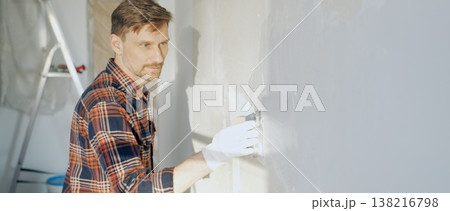 Male construction worker wearing protective gloves smoothing plaster onto wall surface during home renovation using professional trowel tool Male construction worker wearing protective gloves smoothing plaster onto wall surface during home renovation using professional trowel tool 138216798
