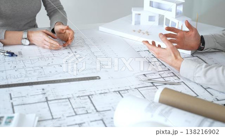 Architects collaborating on building plans, discussing construction blueprints, designing a modern house model, and planning future architectural projects together, close up 138216902