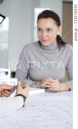 Architects collaborating on building project, discussing architectural model and blueprints on office table during creative planning and design session, close up 138216910