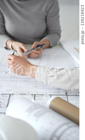 Architects discussing architectural blueprints and a building model on a white desk, planning a new construction project and developing innovative design solutions collaboratively, close up Architects discussing architectural blueprints and a building model on a white desk, planning a new construction project and developing innovative design solutions collaboratively, close up 138216923