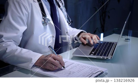 Medical professional wearing a white lab coat and stethoscope. Simultaneously typing patient data on a laptop keyboard and writing notes on a clipboard Medical professional wearing a white lab coat and stethoscope. Simultaneously typing patient data on a laptop keyboard and writing notes on a clipboard 138216926
