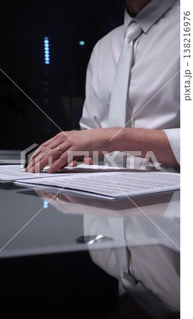 Man in white shirt reviewing legal documents, checking details of a contract with a magnifying glass on a dimly lit desk. Audit, business and overworking concepts 138216976