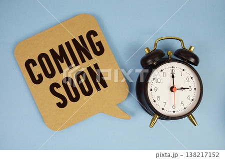 Coming Soon text with alarm clock on blue background 138217152
