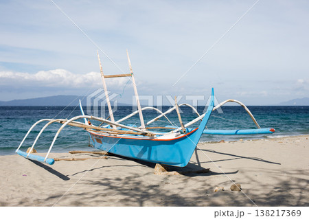 Traditional outrigger fishing boat on sandy shore by deep blue ocean Traditional outrigger fishing boat on sandy shore by deep blue ocean 138217369