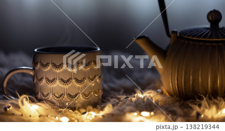 Teapot and cup on a blurred background in the dark with garlands. 138219344