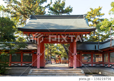 Grand red gate of a traditional Japanese Shinto shrine, surrounded by lush pine trees under a clear sky. A scene showcasing historical architecture and peaceful religious culture in Japan. 138219756