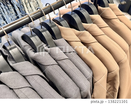 New stylish classic cut jackets in pastel shades are hanging on hangers in a clothing store 138221101