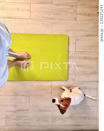 A girl stands on a lemon-colored yoga mat with her pet, a Jack Russell Terrier A girl stands on a lemon-colored yoga mat with her pet, a Jack Russell Terrier 138221241