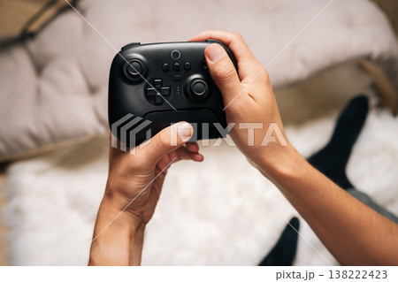 Top view of gamer hands holding modern black wireless video game controller, immersed in playing during leisure time, enjoying competitive gameplay and digital entertainment at home in weekend. Top view of gamer hands holding modern black wireless video game controller, immersed in playing during leisure time, enjoying competitive gameplay and digital entertainment at home in weekend. 138222423