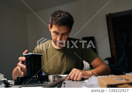 Portrait of computer technician male installing CPU cooler onto motherboard, performing maintenance and repair work on desktop computer in dark workshop. Concept of computer hardware, repairing. 138222427