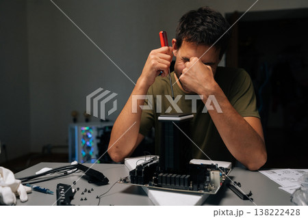 Laughing technician male installing CPU cooler onto motherboard with screwdriver, conducting maintenance and upgrades on desktop computer for improved performance and efficiency. 138222428