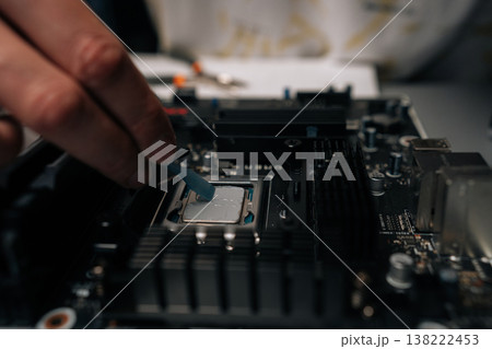 Technician applying thermal paste on computer processor, spreading precise layer for efficient cooling and improved performance during hardware maintenance. Concept of computer hardware, repairing. 138222453