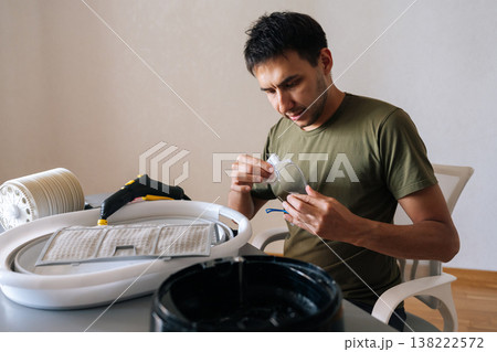 Man carefully cleaning protective glasses, preparing for household chores, with disassembled humidifier parts and cleaning tools on table. Concept of domestic work, housekeeping and household. 138222572