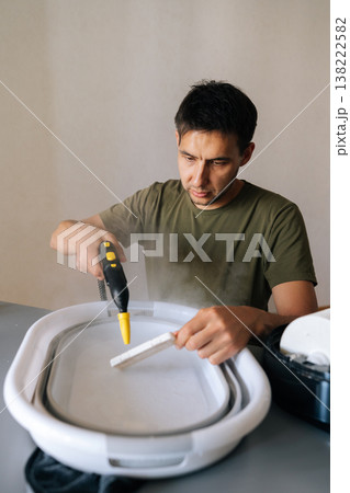 Homemaker male cleaning humidifier filter using steam cleaner, submerging filter in water basin for sanitizing, ensuring optimal indoor air quality and respiratory health. Concept of healthy lifestyle Homemaker male cleaning humidifier filter using steam cleaner, submerging filter in water basin for sanitizing, ensuring optimal indoor air quality and respiratory health. Concept of healthy lifestyle 138222582