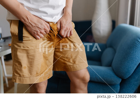 Cropped shot of unhealthy young man grappling with urinary incontinence, anxiously clutching wet pants as navigates discomfort and embarrassment of situation. Concept of healthy lifestyle. Cropped shot of unhealthy young man grappling with urinary incontinence, anxiously clutching wet pants as navigates discomfort and embarrassment of situation. Concept of healthy lifestyle. 138222606
