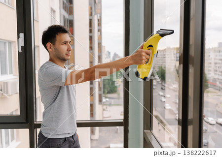 Side view of cleaning service employee using cordless vacuum cleaner to wash windows in high-rise building, ensuring streak-free shine and maintaining clear view. Concept of hygiene, cleanliness 138222617
