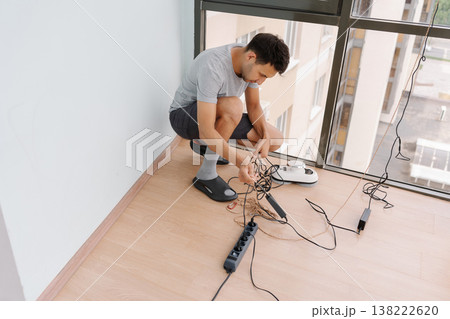 Window cleaner male untangling cables and preparing automatic robot for efficiently cleaning windows of high-rise building, showcasing modern technology and professional maintenance skills 138222620