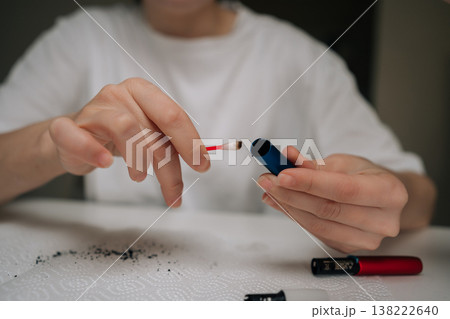 Woman cleaning electronic cigarette mouthpiece with cotton swab, removing residue for hygiene and maintenance in focused, close-up domestic self-care routine. 138222640