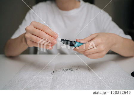 Cropped view of hands disassembling blue e-cigarette over paper towel with dark residue, showing detailed cleaning and maintenance of heat-not-burn vaping device for hygiene and upkeep. Cropped view of hands disassembling blue e-cigarette over paper towel with dark residue, showing detailed cleaning and maintenance of heat-not-burn vaping device for hygiene and upkeep. 138222649