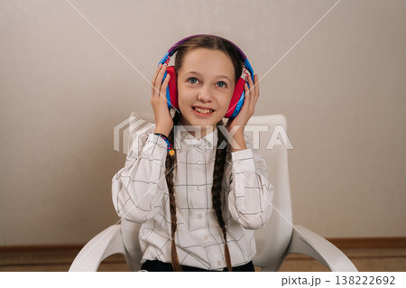 Portrait of cute young girl with braided pigtails enjoying leisure time, listening to audio content through colorful wireless headphones and smiling at the camera. 138222692