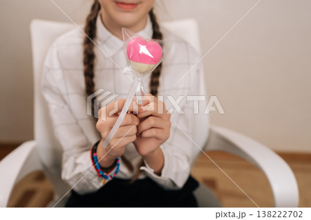 Close-up cropped shot of young girl with braided hair presenting heart shaped candy, embodying sweetness and simple happiness during her childhood years, perfect for themes of joy and innocence. Close-up cropped shot of young girl with braided hair presenting heart shaped candy, embodying sweetness and simple happiness during her childhood years, perfect for themes of joy and innocence. 138222702