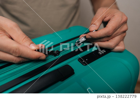 Close-up cropped shot of person securing a teal suitcase zipper and integrated combination lock, demonstrating travel readiness and protection of valuables during a holiday or relocation. 138222779