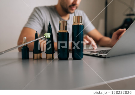 Cropped shot of male seller typing on laptop, managing online e-commerce business of cosmetic products with various skincare beauty tubes and bottles on desk, preparing for sale. 138222826