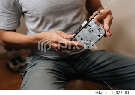 Handyman examining internal door lock mechanism, holding metal components while preparing for installation or repair, highlighting attention to detail and craftsmanship in home maintenance. 138222830