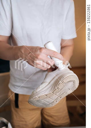 Vertical cropped shot of unrecognizable person using bottle of shoe whitener and painting scuffed surface of dirty white sneaker, illustrating process of cleaning, recoloring, and restoring footwear. Vertical cropped shot of unrecognizable person using bottle of shoe whitener and painting scuffed surface of dirty white sneaker, illustrating process of cleaning, recoloring, and restoring footwear. 138222861