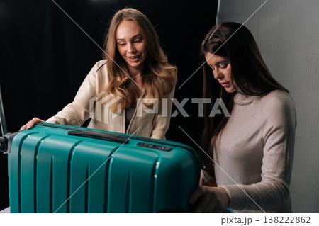 Two young women packing bright suitcase, handling travel essentials and preparing for trip, embodying travel preparation and friendship. Concept of organization and travel essentials. 138222862
