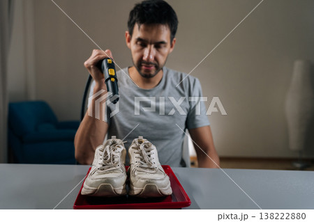 Portrait of young bearded man steam cleaning dirty white sneakers on red tray, restoring bright, fresh appearance while demonstrating careful at home shoe care and stain removal routine. Portrait of young bearded man steam cleaning dirty white sneakers on red tray, restoring bright, fresh appearance while demonstrating careful at home shoe care and stain removal routine. 138222880