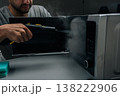 Close-up of man cleaning and sanitizing microwave oven with steam cleaner device, eliminating germs and tough stains, maintaining hygiene in kitchen at home, dark room. 138222906