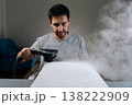 Portrait of young adult man using handheld steam cleaner to sanitize and refresh pillow through chemical-free deep cleaning, ensuring clean and hygienic sleeping space and preventing allergens. 138222909